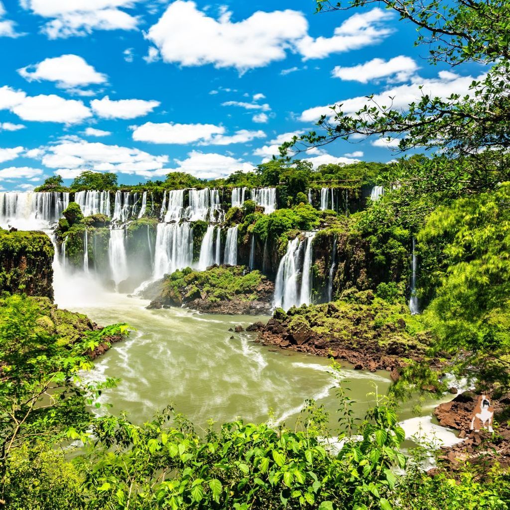 Waterfalls flow against a bright blue sky with white clouds