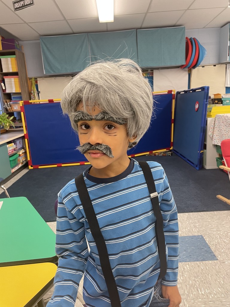 A child wears "old person makeup" with a gray wig and fake eyebrows and mustache. 